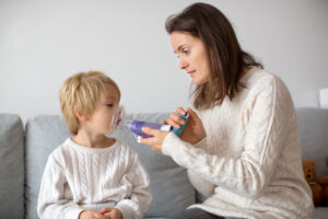 Mother, helping little toddler child with inhaler with spacer, at home